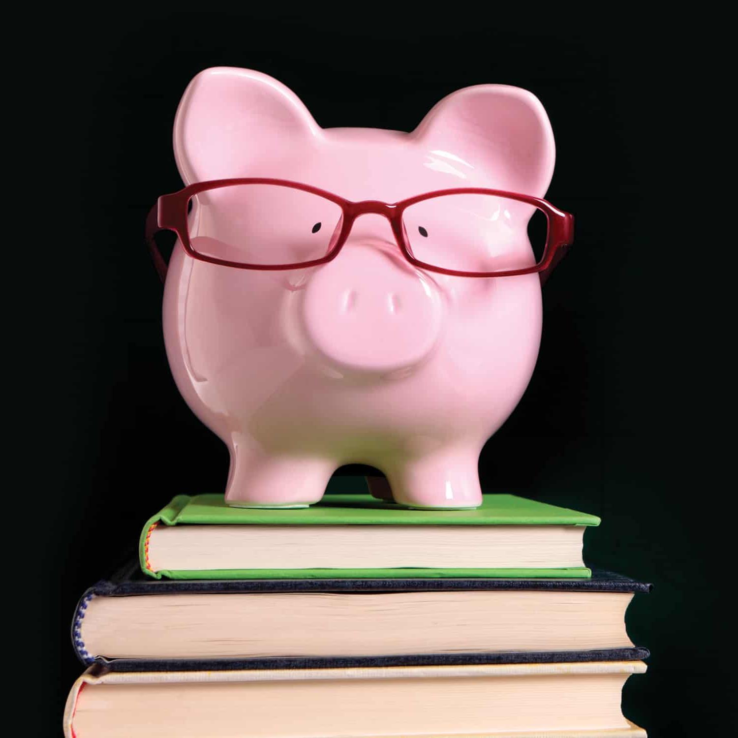 pink piggy bank wearing red glasses on stack of books
